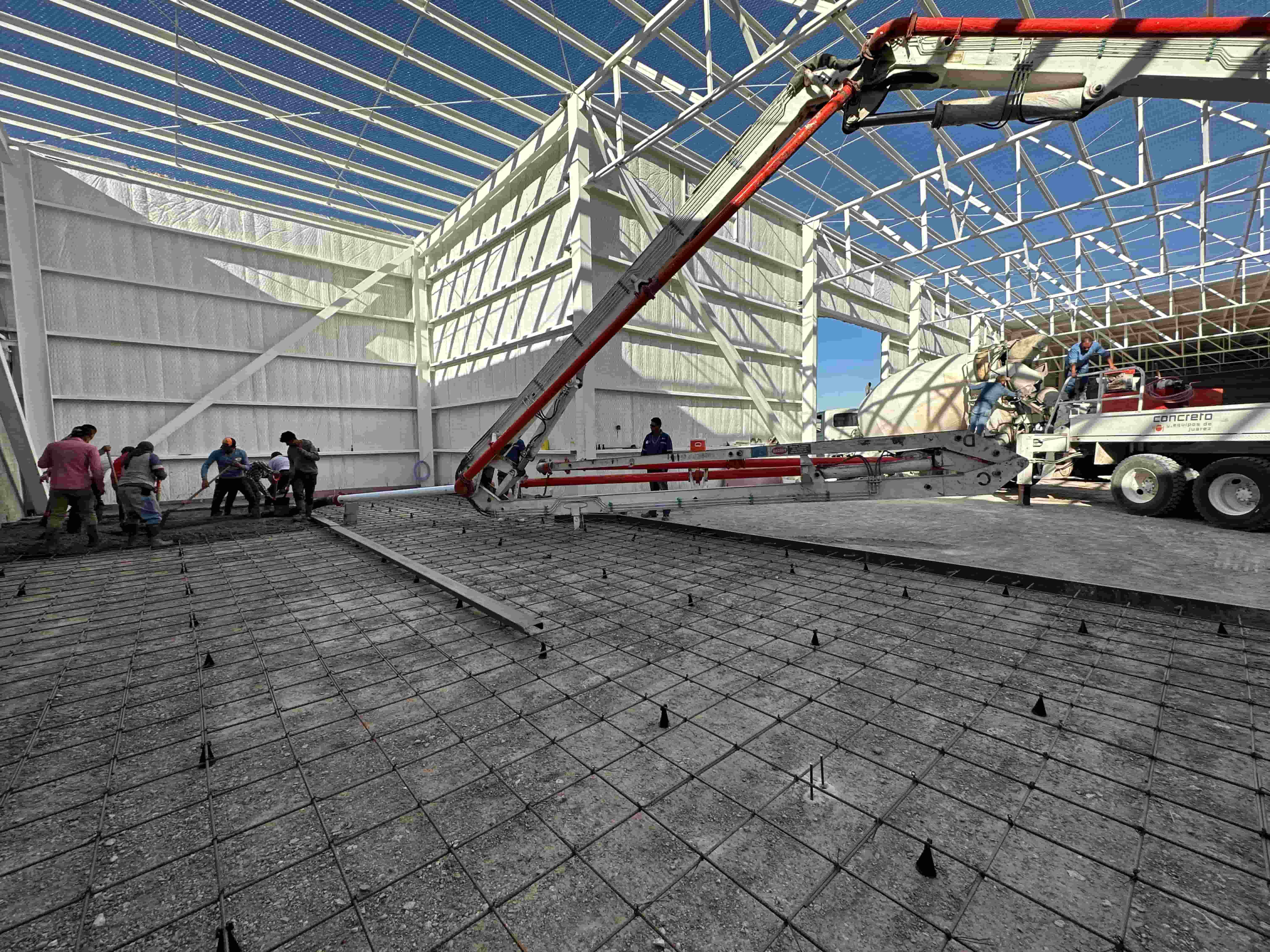 Interior de nave industrial mostrando el colado de piso de concreto con bomba pluma bajo estructura metálica